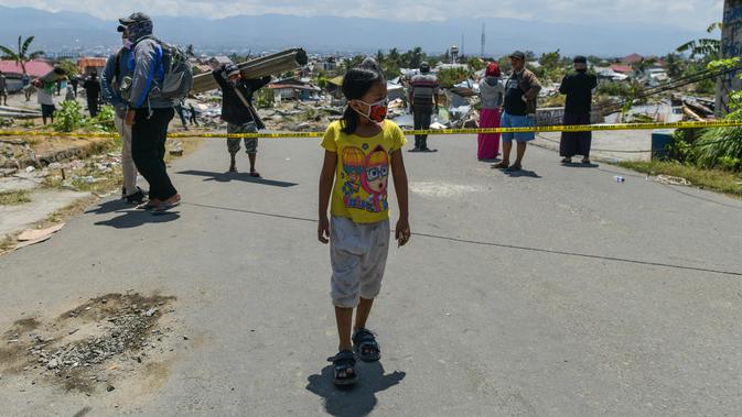Seorang anak yang mengenakan topeng wajah berjalan melewati puing-puing di desa Perumnas Balaroa, Palu, Selasa (2/10). Data terbaru BNPB menunjukkan, korban tewas akibat tsunami dan gempa di Sulawesi Tengah sudah mencapai 1.347 orang. (AFP/Mohd RASFAN)