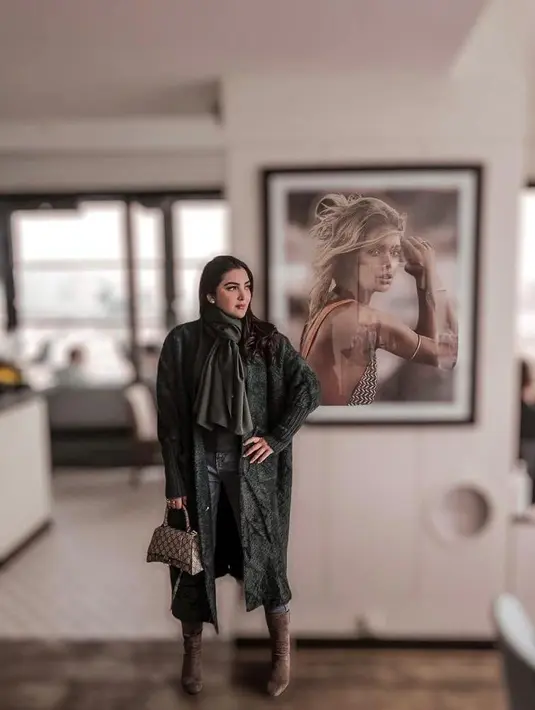 Gaya liburan lainnya yang bisa dijadikan inspirasi adalah look Ashanty berikut ini. Padukan long coat dengan celana jeans, dan syal warna hijau army. Sepatu boots warna cokelat sebagai aksesori bikin look makin standout (Instagram/ashanty_ash).