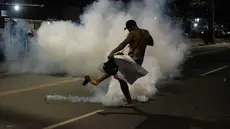 Seorang penduduk favela Cidade de Deus (Kota Tuhan) menendang tabung gas air mata yang ditembakkan oleh polisi selama protes di kota kumuh di Rio de Janeiro, Brasil, pada 7 Agustus 2023. (AFP/Tercio Teixeira)