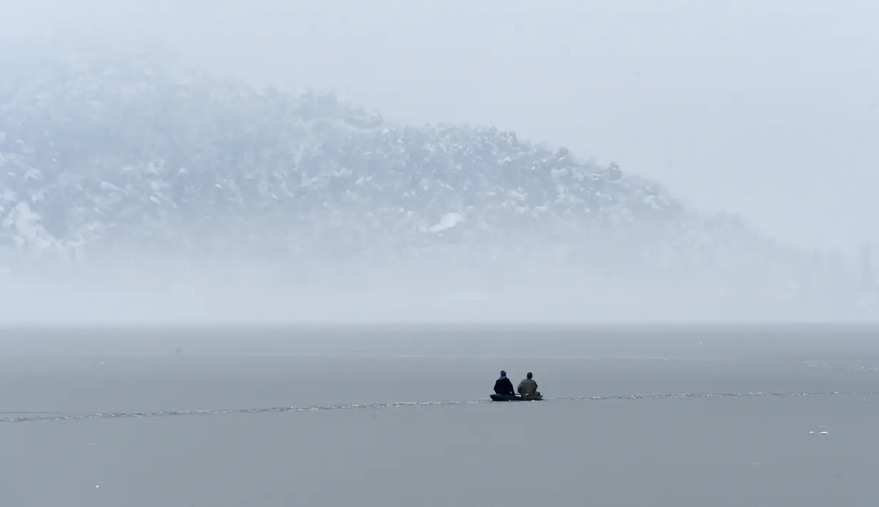 Dua pria menaiki perahu di dekat bagian beku danau Dal setelah hujan salju lebat di Srinagar (16/1/2020). Lapisan tipis es menutupi perairan Danau Dal di Srinagar. (AFP Photo/Tauseef Mustafa)
