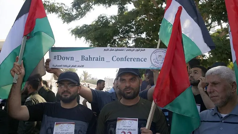 Warga Palestina di Kota Gaza pada 24 Juni 2019, mengibarkan bendera nasional dan memegang spanduk yang mengecam konferensi Perdamaian untuk Kemakmuran yang dipimpin AS di Bahrain. (MOHAMMED ABED / AFP)