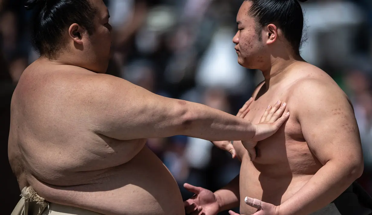 <p>Para pegulat sumo melakukan pemanasan sebelum "turnamen sumo besar nazar", sebuah pameran sumo seremonial, di halaman Kuil Yasukuni di Tokyo pada 17 April 2023. (AFP/Philip Fong)</p>