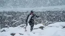 Seorang peselancar berjalan menerobos derasnya hujan salju di Lofoten Islands, Norwegia, (11/3/2018). Suhu udara minus 13°C dan suhu diatas air sekitar 4°C. (AFP/Oliver Morin)