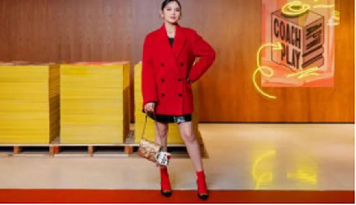 Ia memilih short wool coat merah yang memikat, dipadukan dengan rok mini berbahan patent leather yang kesan edgy pada penampilannya. [Foto: Coach]
