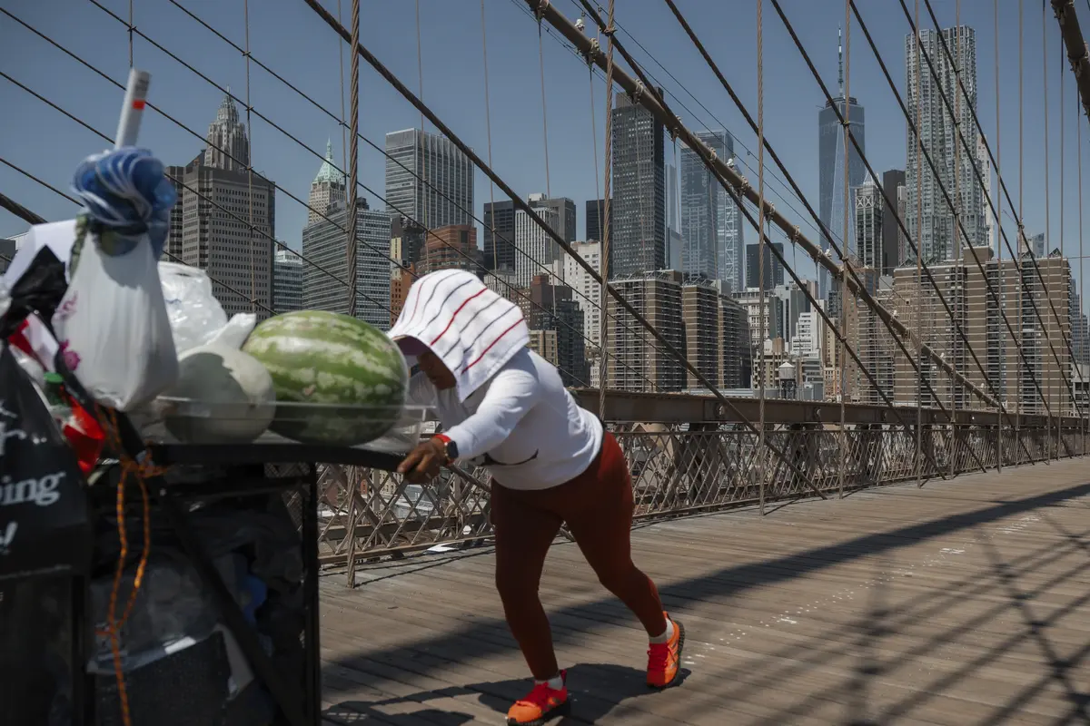 Seorang penjual buah mendorong gerobaknya di Jembatan Brooklyn saat gelombang panas di New York. (AP Photo/Olga Fedorova)