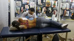 Seorang seniman terlihat serius menato seorang perempuan dibagian samping dadanya saat Festival Internasional Tattoo Week Rio 2016 ketiga di Rio de Janeiro, Brasil, (22/1/2016). (REUTERS/Pilar Olivares)