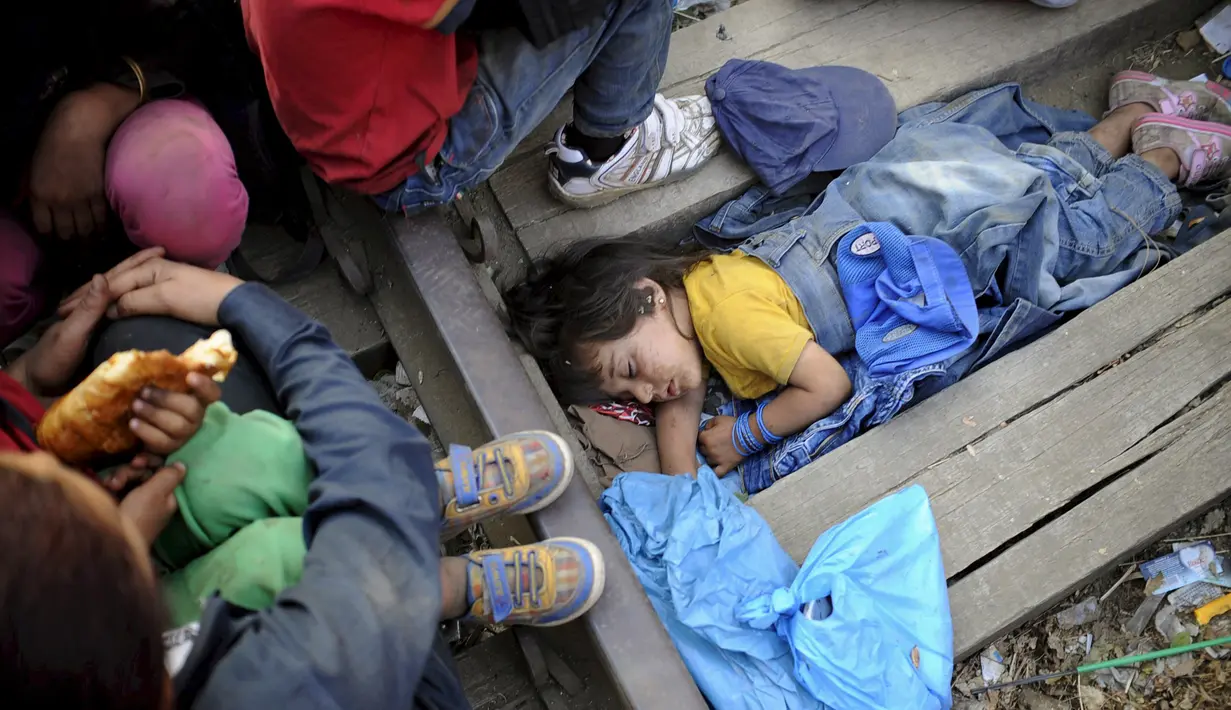 Bocah empat tahun bernama Rashida dari Suriah tidur di sela - sela balok kayu saat mereka menunggu di garis perbatasan Makedonia dan Yunani untuk masuk ke Makedonia, 20 Agustus 2015. (REUTERS/Ognen Teofilovski)