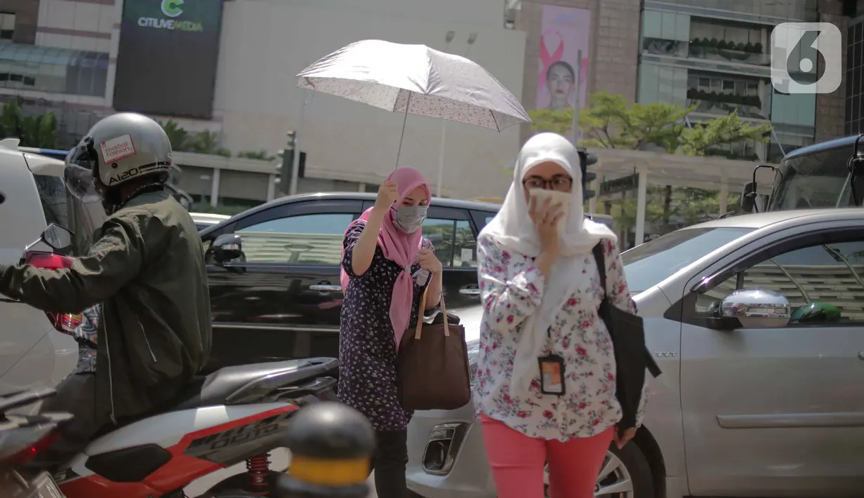 Seorang wanita menggunakan payung menyebrang selama gelombang panas di Jakarta, Selasa (22/10/2019).  BMKG memprediksi wilayah Indonesia akan mengalami panas selama kurang lebih satu minggu ini. Hal ini dikarenakan matahari yang berada dekat dengan jalur khatulistiwa. (Liputan6.com/Faizal Fanani)