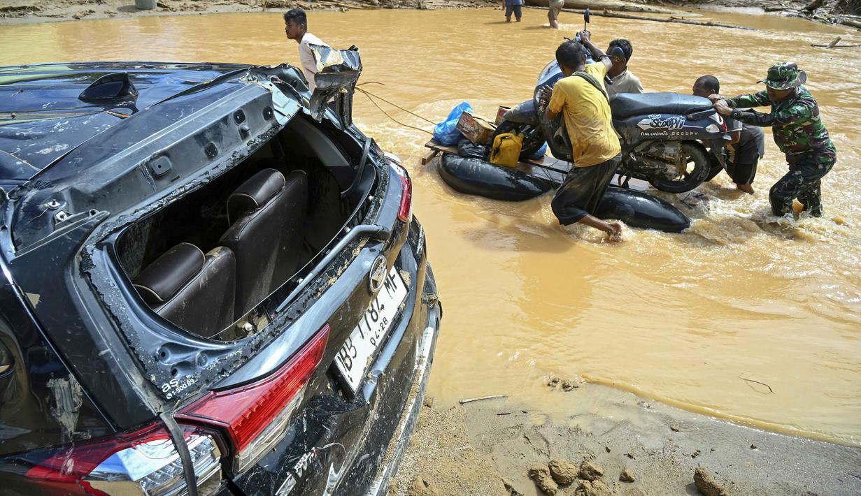 Warga terpaksa bertahan dengan persediaan seadanya. Hingga Selasa (2/12/2025), 86 orang dinyatakan meninggal dunia dan 99 lainnya belum ditemukan sejak banjir bandang dan longsor yang melanda Kabupaten Tapanuli Tengah. Tampak dalam foto, warga desa mendorong sepeda motor di atas rakit darurat di sepanjang jalan yang tergenang akibat banjir bandang di Desa Tukka, Tapanuli Tengah, Sumatera Utara, pada 2 Desember 2025. (YT HARIONO/AFP)