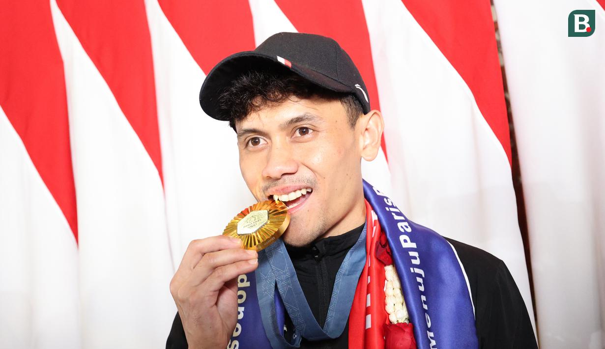 <p>Veddriq Leonardo menggigit medali emas Olimpiade Paris 2024 usai tiba di Bandara Internasional Soekarno-Hatta, Tangerang, Selasa (13/08/2024). (Abdul Aziz/Bola.com)</p>