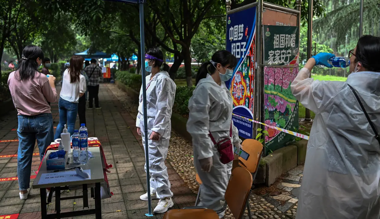 Petugas berdiri di sebelah warga yang menunggu untuk tes virus corona di lingkungan di Wuhan, provinsi Hubei, Jumat (15/5/2020). Tes massal yang ditargetkan dalam 10 hari ini akibat adanya pasien Virus Corona baru di Wuhan, setelah sebulan lebih tidak ada laporan kasus baru. (Hector RETAMAL/AFP)