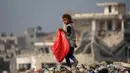 Seorang anak pengungsi Palestina membawa plastik besar untuk diisi dengan barang-barang yang ditemukan di tumpukan sampah, di kamp pengungsi al-Bureij di Jalur Gaza tengah pada 10 November 2024. (Eyad BABA/AFP)