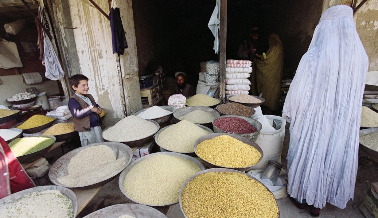 Seorang wanita mengenakan burqa yang diwajibkan Taliban saat memasuki toko berbagai jenis beras dan biji-bijian di Kabul, Afghanistan, 17 November 1996. (EMMANUEL DUNAND/AFP)