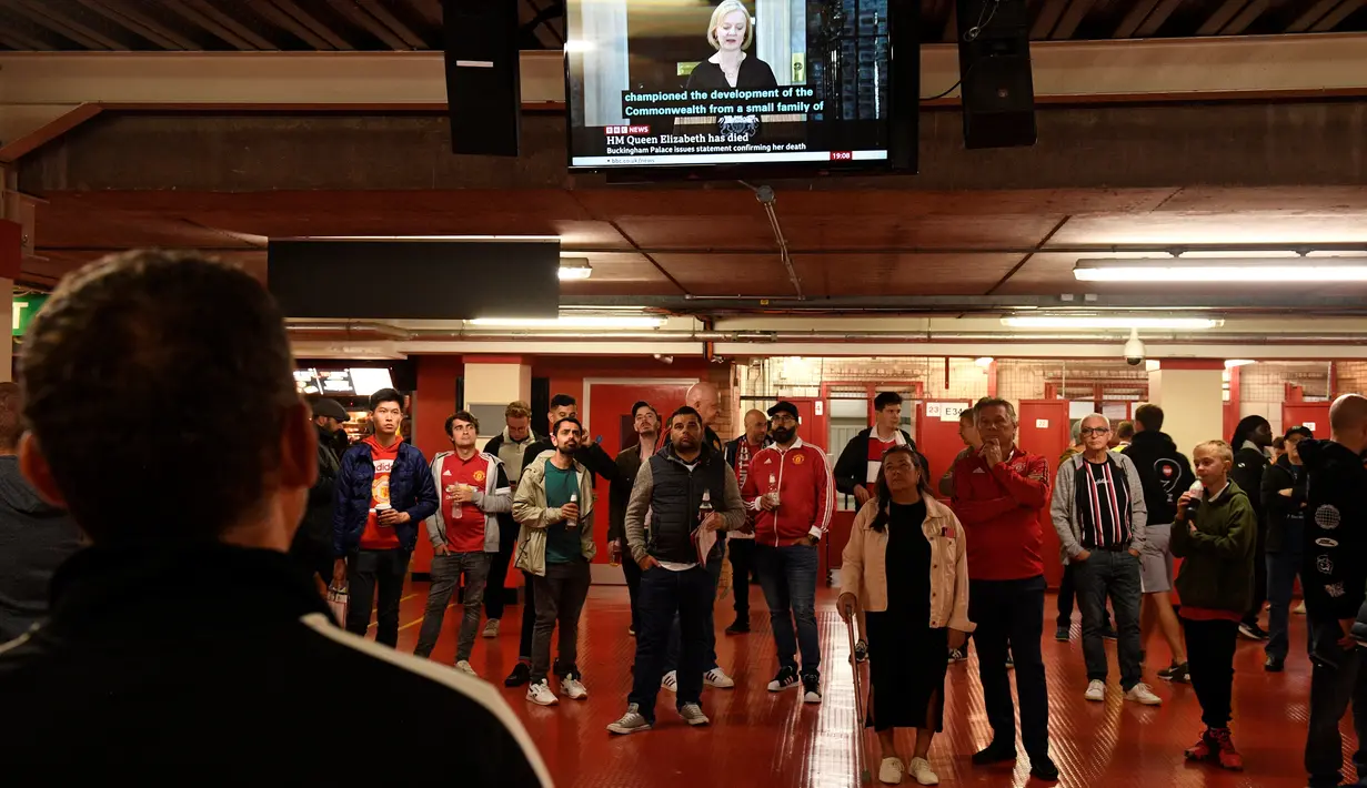 Fans mendengarkan televisi saat Perdana Menteri Inggris Liz Truss membacakan pernyataan di Downing Street, menyusul berita bahwa Ratu Elizabeth II telah meninggal, menjelang pertandingan sepak bola Grup E UEFA Europa League antara Manchester United dan Real Sociedad, di stadion Old Trafford, di Manchester, pada 8 September 2022. (AFP/Oli Scarff)