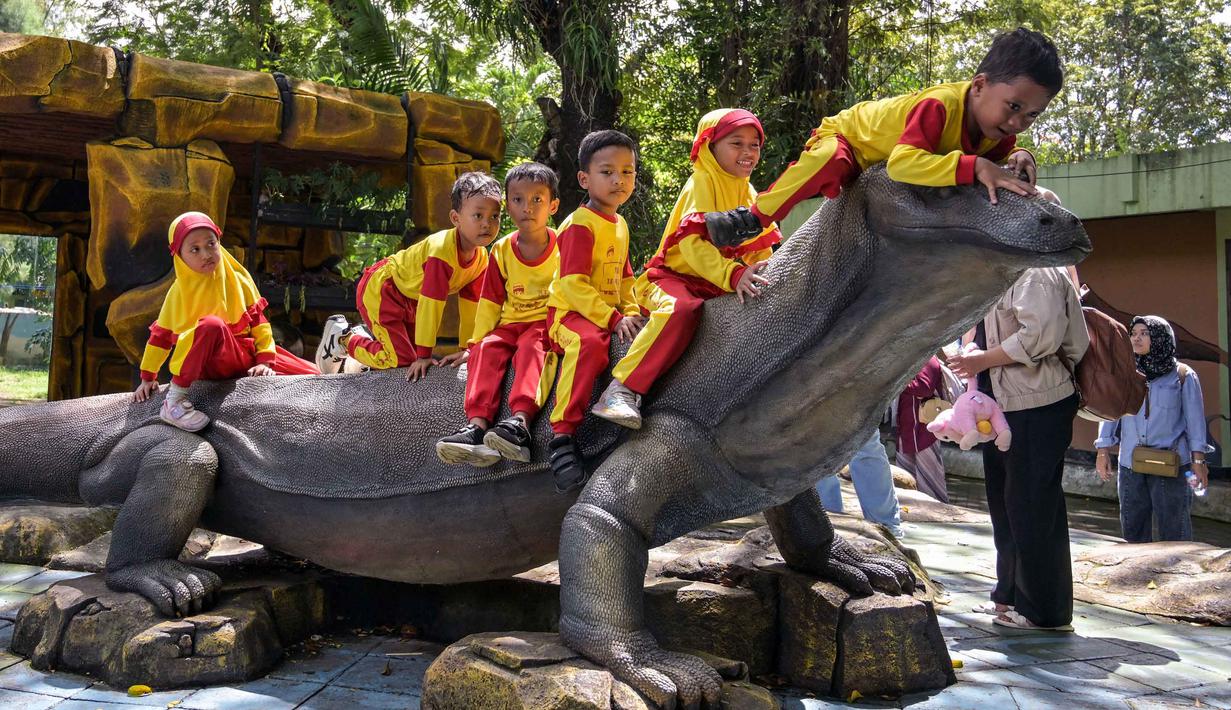Beberapa murid taman kanak-kanak duduk di atas patung komodo di Kebun Binatang Surabaya, Jawa Timur, pada Rabu 29 April 2026. (JUNI KRISWANTO/AFP)