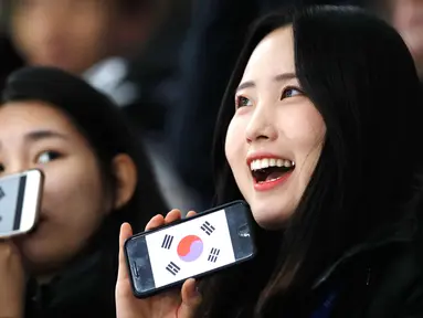 Dua wanita Fans Skating memperlihatkan ponsel mereka yang bergambar bendera Korea Selatan sebelum pertandingan balapan speed skater 1.500 meter pada Olimpiade Musim Dingin 2018 di Gangneung Oval, Korea Selatan, Selasa, (13/2). (AP Photo / Vadim Ghirda)