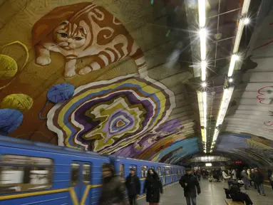 Penumpang melewati kereta di bawah mural yang menghiasi dinding stasiun metro bawah tanah kota di Kyiv, Ukraina, Rabu, (29/1/2020). (AP Photo / Efrem Lukatsky)