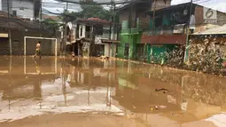 Warga melintas di lapangan futsal yang diselimuti sampah dan lumpur di kawasan Rawajati, Jakarta, Selasa (6/2). Banjir yang merendam kawasan tersebut menyebabkan lumpur dan sampah mengendap di setiap sudut. (Liputan6.com/Immanuel Antonius)