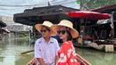 Ririn Ekawati bersama suami saat mengunjungi sebuah kampung terapung dengan menggunakan perahu. Ririn tampil cantik mengenakan busana berwarna merah motif kembang dan topi di kepalanya. (Instagram/ririnekawati)