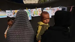 Dalam coretannya, mereka mengungkap penderitaan, kengerian, dan harapan mereka akan terjadinya perdamaian. Tampak dalam foto, orang-orang yang membawa anak-anak melihat pameran di sebuah sekolah yang diubah menjadi tempat penampungan bagi pengungsi Palestina di kawasan Al-Rimal, Kota Gaza, pada 5 November 2025. (Omar AL-QATTAA/AFP)