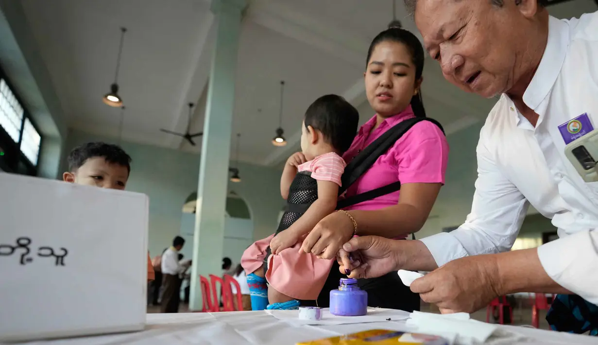 Tahap pertama pemilu Myanmar digelar hari ini, Minggu 28 Desember 2025, dimulai pukul 06.00 waktu setempat di sejumlah daerah, termasuk Yangon, Mandalay, dan ibu kota Naypyidaw. Tampak dala foto, seorang pemilih, sambil menggendong anaknya, mencelupkan jarinya ke dalam botol tinta setelah memberikan suara di tempat pemungutan suara di Yangon, Myanmar, Minggu, 28 Desember 2025, (AP Photo/Thein Zaw)