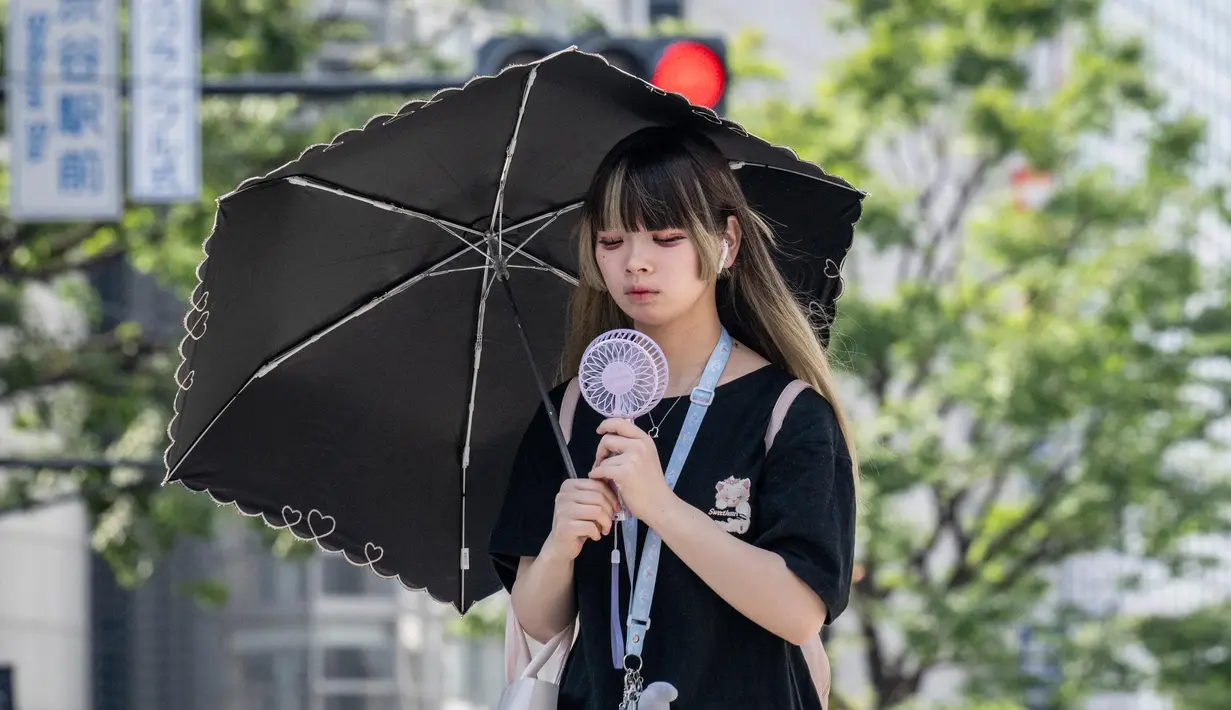 Seorang wanita menggunakan payung untuk berlindung dari sinar matahari saat berjalan di sepanjang jalan di Tokyo pada 19 September 2024. (Yuichi YAMAZAKI/AFP)