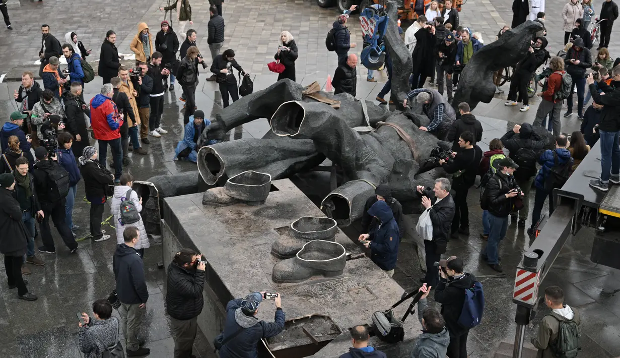 <p>Wartawan dan penduduk setempat melihat monumen era Soviet untuk persahabatan antara Rusia dan Ukraina yang dibongkar oleh pekerja, di tengah invasi Moskow di Kiev, Ukraina, Selasa (26/4/2022). Patung itu terletak di bawah 'Lengkungan Persahabatan Rakyat' titanium raksasa, yang didirikan pada 1982 untuk memperingati ulang tahun ke-60 Uni Soviet. (Genya SAVILOV / AFP)</p>