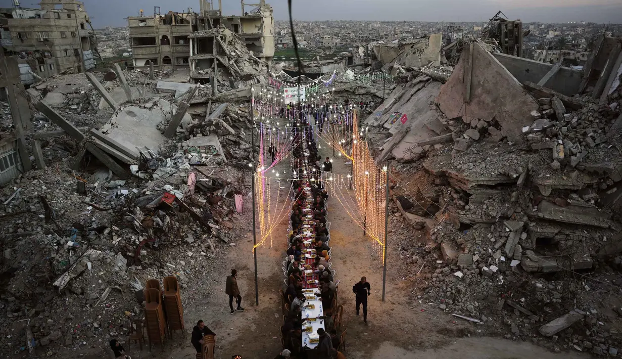 Dekorasi sederhana khas Ramadan tetap dipasang oleh warga Palestina di Gaza untuk menghadirkan suasana hangat dan solidaritas. Tampak dalam foto, warga Palestina duduk di meja panjang di tengah reruntuhan bangunan yang hancur untuk berbuka puasa bersama, selama bulan suci Ramadan di Khan Younis, Jalur Gaza, Kamis 19 Februari 2026. (AP Photo/Abdel Kareem Hana)