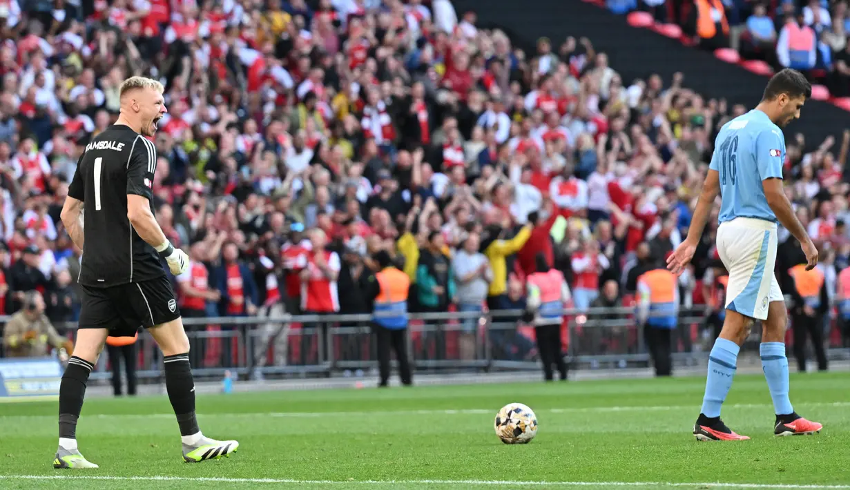 Kiper Arsenal, Aaron Ramsdale, melakukan selebrasi setelah berhasil menghalau tendangan penalti pemain Manchester City, Rodri, pada laga Community Shield di Stadion Wembley, London, Minggu (6/8/2023). Arsenal mengalahkan Manchester City 4-1 lewat adu penalti setelah bermain imbang 1-1 selama 90 menit. (AFP/Glyn Kirk)