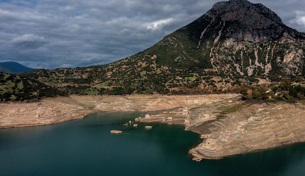 Foto ini menunjukkan sisa-sisa rumah yang muncul kembali ketika permukaan danau buatan Mornos menurun akibat kekeringan, di desa Kallio, sekitar 240 km barat laut Athena, Yunani pada 3 November 2025. Kemunculan kembali desa tersebut disebabkan oleh kekeringan parah dan tingkat air danau yang menurun drastis ke level terendah dalam beberapa dekade, akibat musim dingin dengan sedikit salju, gelombang panas, dan curah hujan yang rendah di Yunani. (Angelos TZORTZINIS/AFP)