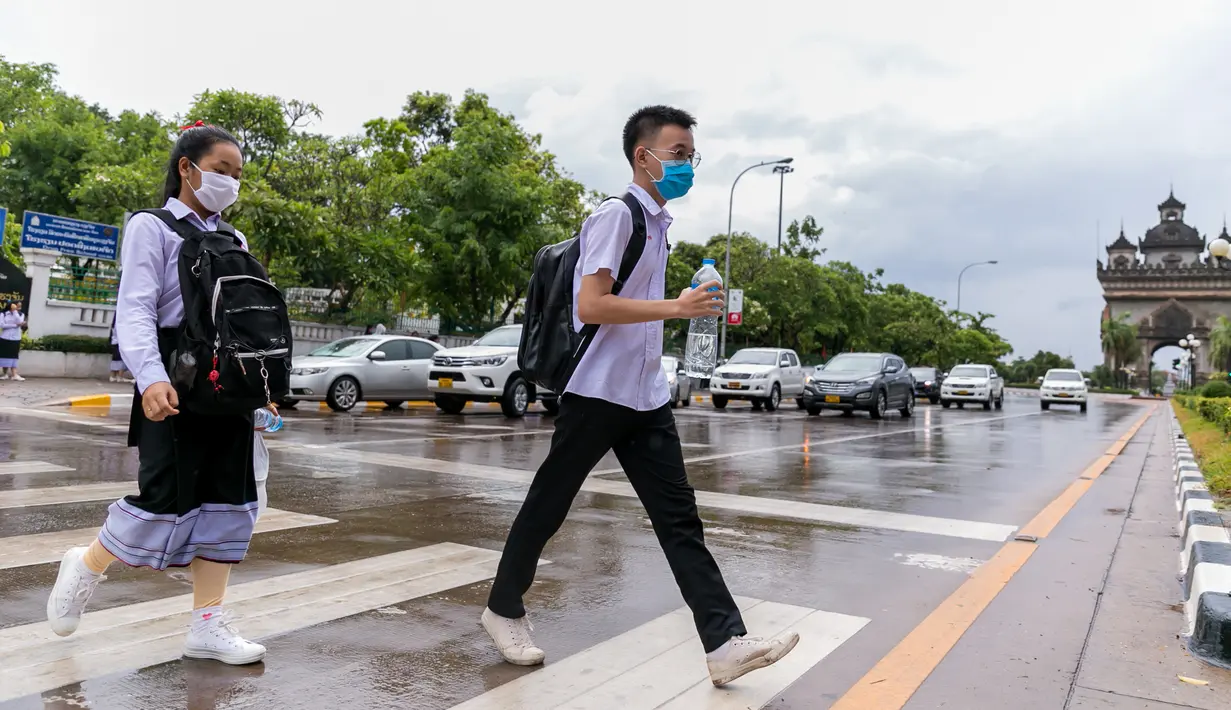 Sejumlah siswa yang mengenakan masker menyeberangi jalan saat pulang sekolah di Vientiane, Laos, Selasa (19/5/2020). Pemerintah Laos telah mengumumkan bahwa semua siswa di negara itu dapat kembali bersekolah mulai 2 Juni mendatang. (Xinhua/Kaikeo Saiyasane)