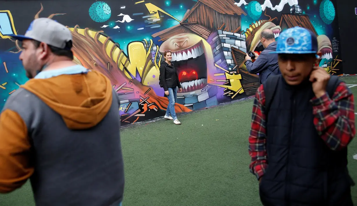Wisatawan berfoto di depan karya seni grafiti pada festival pekan grafiti di Mexico City, Meksiko, Minggu (9/10). Grafiti merupakan salah satu seni jalanan yang populer hingga kini. (REUTERS/Carlos JASSO)