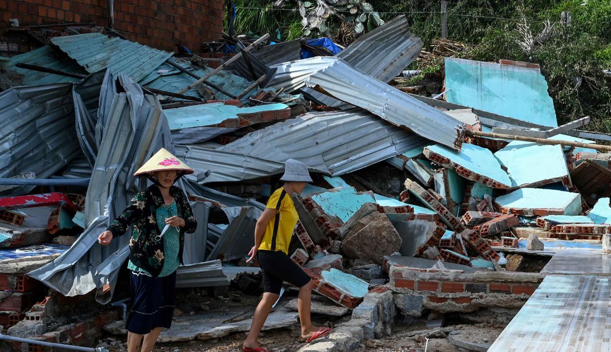 Pemerintah Vietnam telah mengerahkan ratusan ribu tentara untuk membantu evakuasi dan operasi pencarian. Tampak dalam foto, warga berjalan di atas puing-puing bangunan yang hancur akibat angin kencang di desa nelayan Nhon Hai dekat Quy Nhon, Provinsi Gia Lai, Vietnam Tengah, pada Jumat 7 November 2025. (NHAC NGUYEN/AFP)