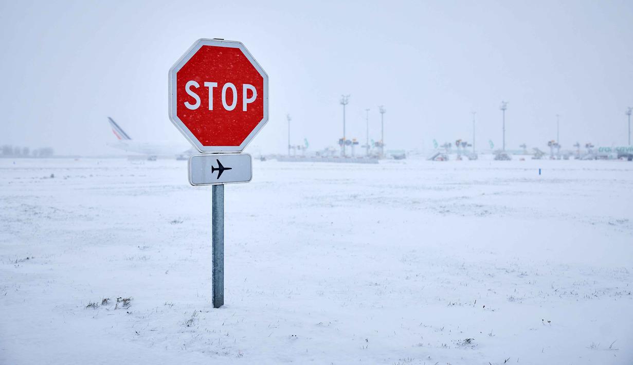 Foto ini menunjukkan rambu berhenti di dekat landasan pacu saat salju menyelimuti landasan, menyebabkan pembatalan penerbangan di Bandara Orly, selatan Paris pada 7 Januari 2026. Cuaca dingin ekstrem dan hujan salju lebat yang melanda sebagian besar wilayah Eropa, menyebabkan gangguan perjalanan yang meluas serta merenggut nyawa enam orang dalam serangkaian insiden terkait cuaca buruk di benua tersebut. (Kiran RIDLEY/AFP)