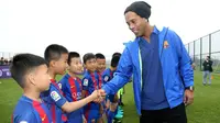Mantan pemain Barcelona, Ronaldinho, menyalami anak-anak saat peluncuran akademi sepak bola Barcelona di China, Jumat (24/2/2017). (AFP/Handout)