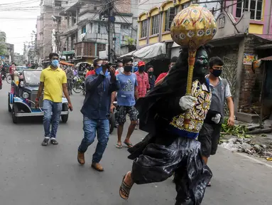Seorang pria berkostum dewa kematian Yamaraj berlari keliling mencari warga yang masih berkeliaran tanpa masker di tengah lockdown di Kolkata, India (24/4/2020). Dalam aksinya, pria tersebut memberikan imbauan kepada warga agar memakai masker di tengah wabah virus corona. (AFP/Dibyangshu Sarkar)