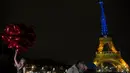 Para turis berpose dengan balon saat Menara Eiffel diterangi dengan warna-warna khas Ukraina untuk menandai peringatan satu tahun invasi Rusia ke negara tersebut, di Paris, Kamis, 23 Januari 2023. Pada 24 Februari 2022 lalu Rusia menginvasi Ukraina dan menandai puncak eskalasi konflik kedua negara sejak 2014 silam. (AP Photo/Christophe Ena)