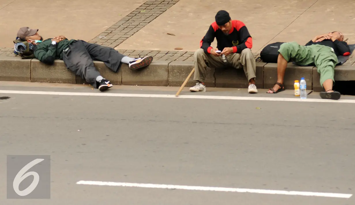Massa aksi damai beristirahat di pinggir Jalan Merdeka Barat jelang bergerak menuju Istana Negara, Jakarta, Jumat (4/11). Massa melakukan aksi di depan Istana Negara menuntut penegakan hukum kasus dugaan penistaan agama. (Liputan6.com/Helmi Fithriansyah)