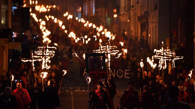 Peserta melakukan pawai sambil membawa obor dalam perayaan Bonfire Night melintasi jalan di Sussex Timur, Inggris, Selasa (5/11/2019). Perayaan tersebut ditujukkan untuk memperingati hari eksekusi Guy Fawkes, yaitu eksekutor yang ditugaskan meledakkan House of Parliament. (Ben STANSALL/AFP)