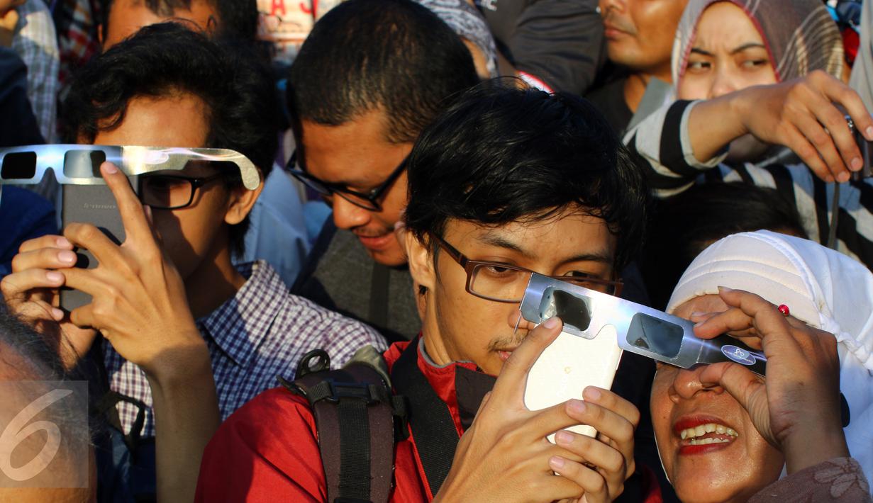 Warga menyaksikan fenomena Gerhana Matahari Total (GMT) menggunakan ponsel di halaman Taman Ismail Marzuki (TIM), Jakarta, Rabu (9/3). Fenomena gerhana matahari 90% bisa diamati selama 2,11 menit. (Liputan6.com/Fery Pradolo)