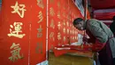 Seorang kaligrafer menulis kuplet musim semi, semacam dekorasi Tahun Baru Imlek, jelang dimulainya Tahun Baru Imlek di sebuah kios di Foshan, Provinsi Guangdong, China, 18 Januari. Kuplet biasanya dipasang melintang di kusen pintu. (Giok Gao/AFP)