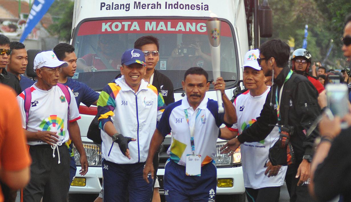 Petinju legendaris Indonesia, Nico Thomas, membawa obor Asian Games XVIII saat melintas di Kota Malang, Jawa Timur, Jumat (20/7/2018). Sebanyak 53 kota di Indonesia akan dilalui oleh obor Asian Games. (Bola.com/Iwan Setiawan)
