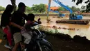 Pengendara motor melintas saat alat berat mengeruk lumpur di Setu Babakan, Jakarta, Selasa (30/6/2020). Pengerukan dilakukan guna mengembalikan kedalaman setu sehingga menambah daya tampungnya. (Liputan6.com/Immanuel Antonius)
