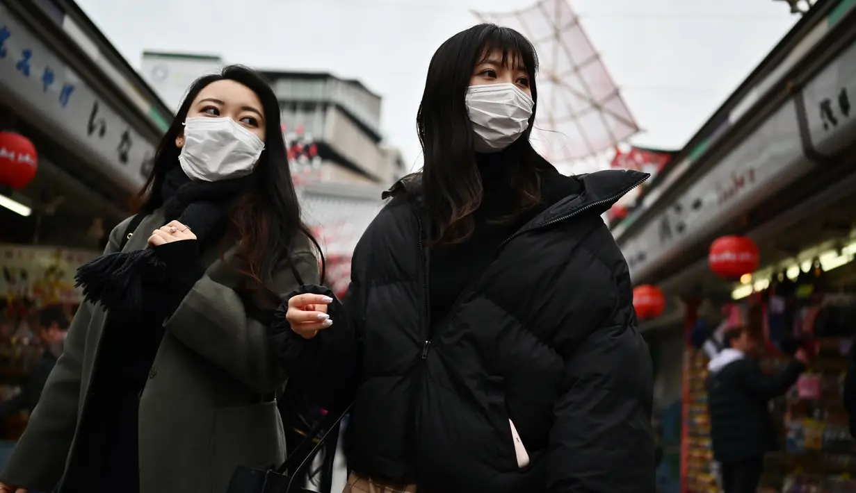 Dua wanita memakai masker berjalan di sepanjang jalan dekat kuil Sensoji di daerah Taito Tokyo (27/1/2020). Masker dipilih sebagai salah satu tindak pencegahan sederhana dari virus dengan karakteristik mirip SARS tersebut. (AFP Photo/Charly Triballeau)