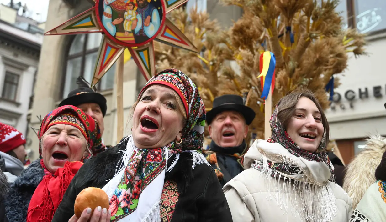 Hingga kini, 'Didukh' masih menjadi elemen budaya yang sangat penting dan masih terus dipraktikkan di Ukraina. Tampak dalam foto, warga yang mengenakan pakaian tradisional dan membawa hiasan tradisional Ukraina 'Didukh' menyanyikan lagu-lagu rohani saat mereka mengikuti prosesi Malam Natal di Lviv pada 24 Desember 2025. (YURIY DYACHYSHYN/AFP)