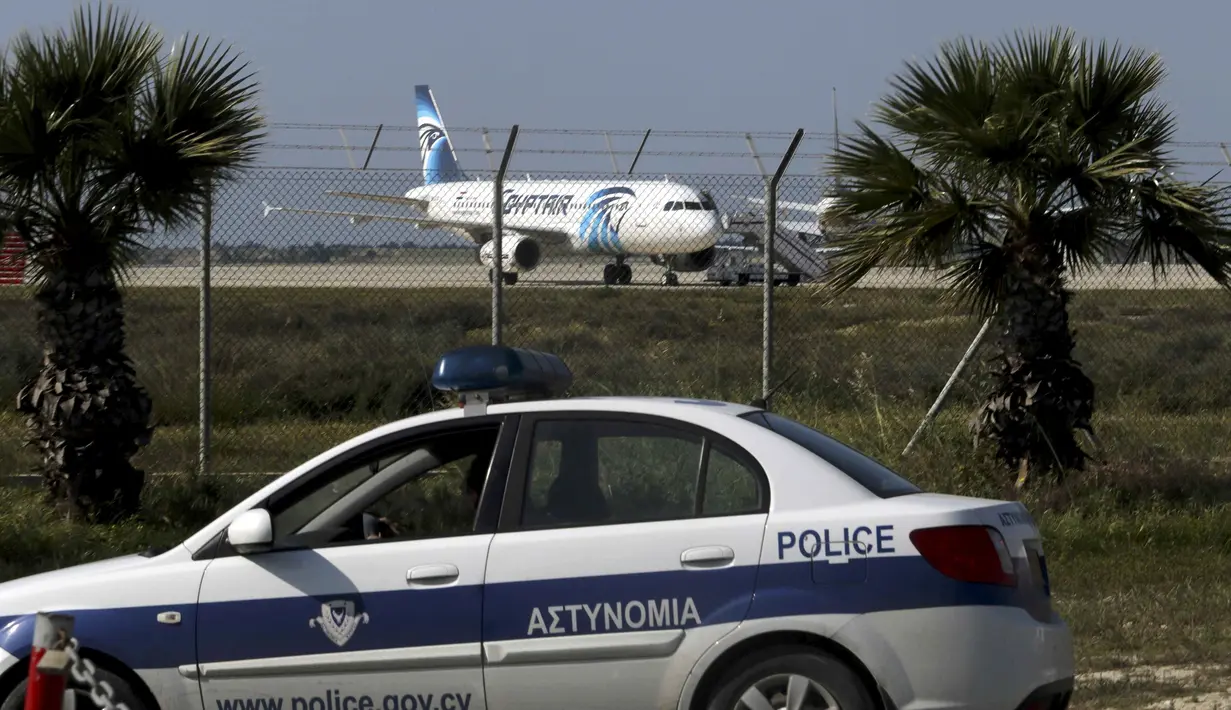 Mobil polisi disiagakan di dekat pesawat milik maskapai Mesir, EgyptAir, yang dibajak dan dipaksa mendarat di Bandara Larnaca, Siprus, Selasa (29/3). Pembajak adalah seorang penumpang yang mengklaim membawa sabuk bahan peledak (REUTERS/Yiannis Kourtoglou)