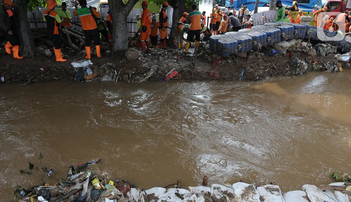 Petugas Suku Dinas Sumber Daya Air (Sudin SDA) Jakarta Timur menutup luapan air dari tanggul menggunakan tumpukan karung-karung pasir. (merdeka.com/Imam Buhori)