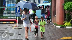 Dua pengojek payung cilik mengikuti  wanita yang memakai jasa ojek payung mereka di Jakarta, Selasa (1/11). Musim hujan membawa berkah bagi anak-anak tersebut karena bisa mendapatkan rezeki lebih dari jasa ojek payung. (Liputan6.com/Angga Yuniar)