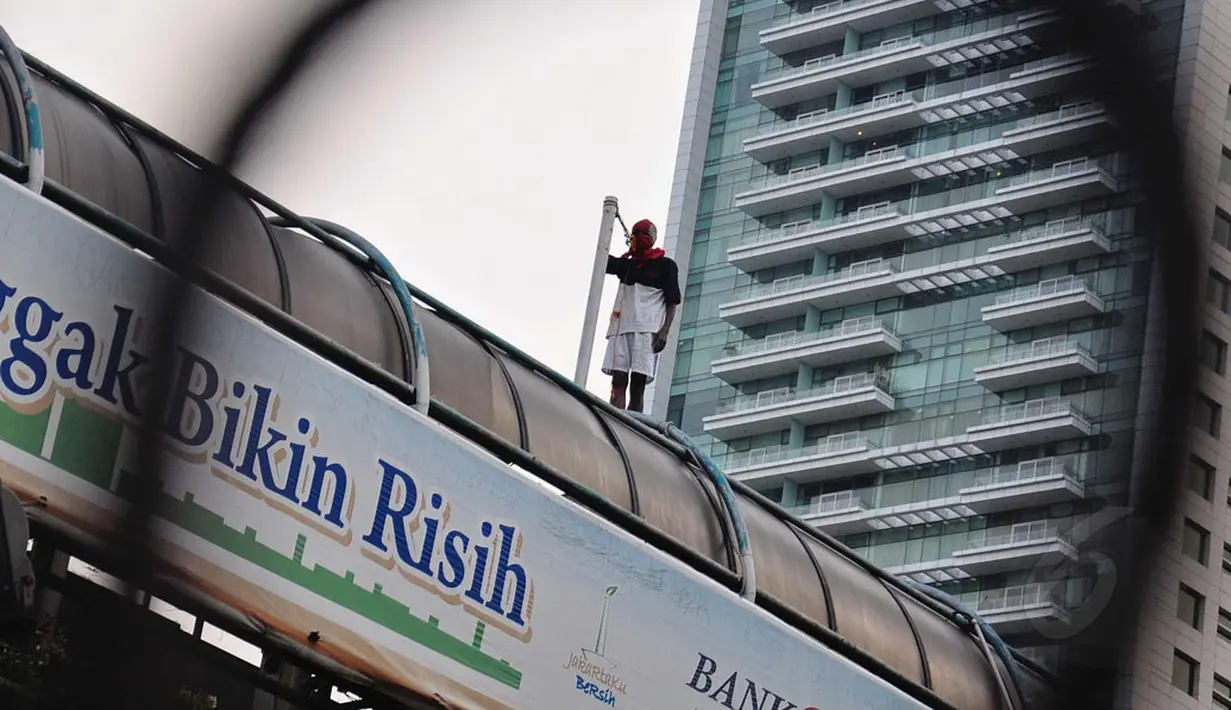 Dengan wajah tertutup, seorang tidak dikenal melakukan aksi unjuk rasa di atas JPO di sekitar Bundaran HI, Jakarta, (25/7/2014). (Liputan6.com/Faizal Fanani)