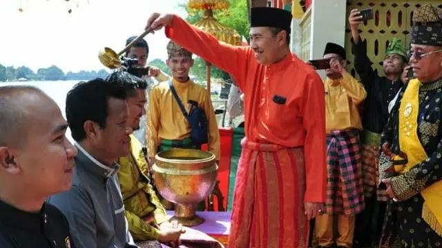Prosesi menyiramkan air berisi ramuan jeruk dan bunga rampai dalam tradisi Balimau Kasi di Provinsi Riau.